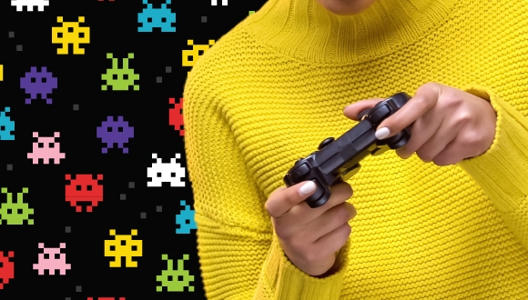 une personne en chandail jaune qui joue avec un contrôleur de jeu, contre un arrière-plan de personnages style "Space Invaders"